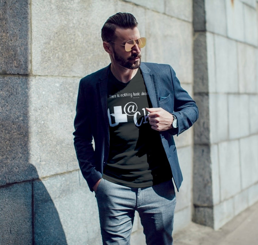 Man wearing a black jacket, asphalt  t-shirt with white graphics, and light blue jeans against a stone wall.
