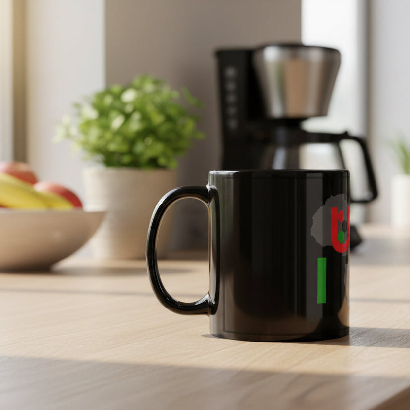 Black mug with a colorful design on a kitchen counter with a coffee maker and fruit bowl in the background.
