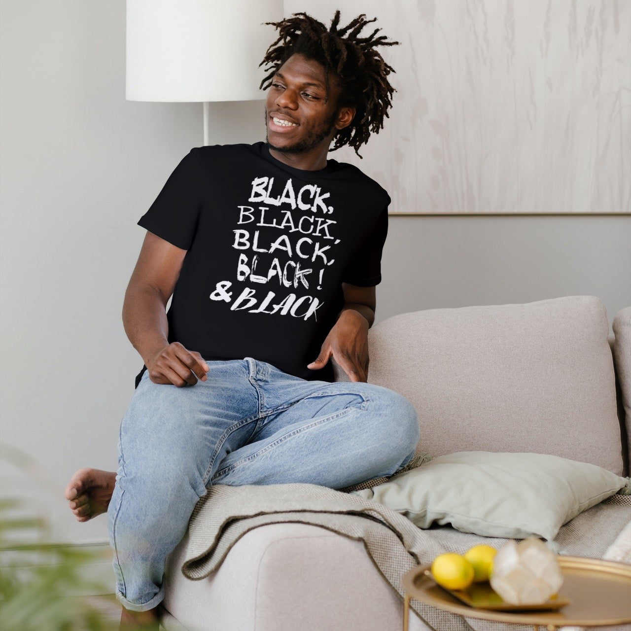 Person sitting on a couch wearing a black graphic  t-shirt with text, in a modern living room.
