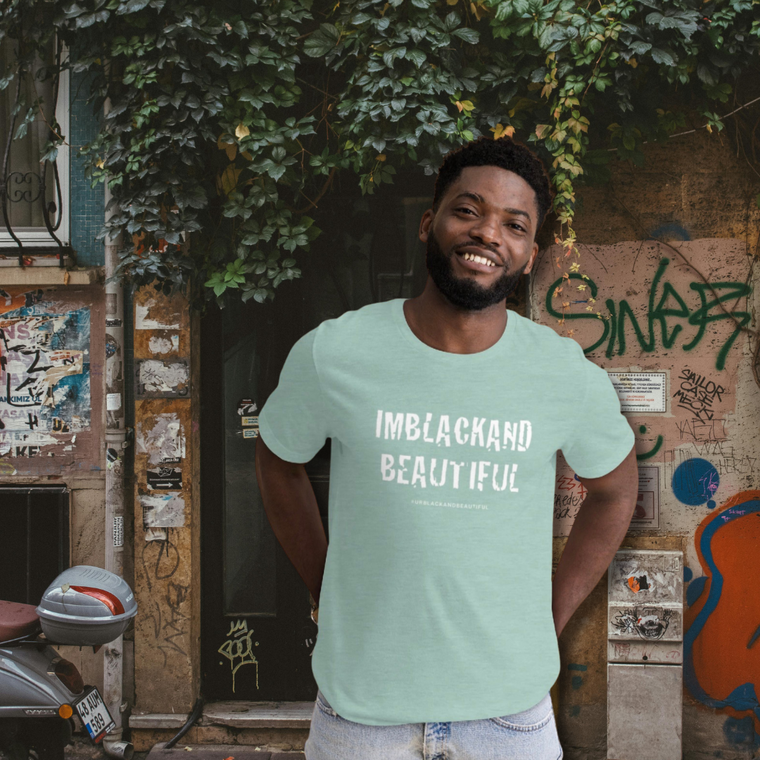 Man wearing a light blue t-shirt with 'IMBLACKAND BEAUTIFUL' text, standing in front of a graffiti-covered wall.