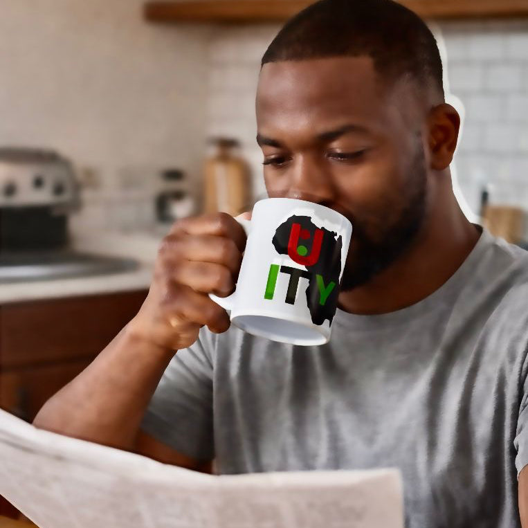 Man drinking from a mug with a colorful design while reading a newspaper in a kitchen.