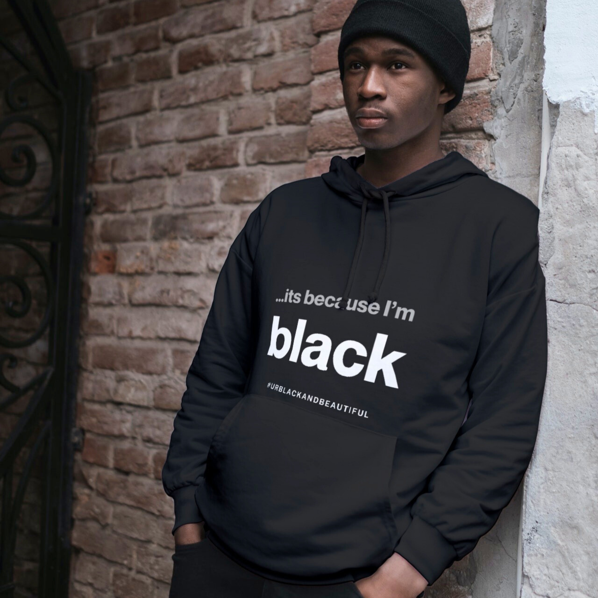 Person wearing a black statement hoodie with text standing against a brick wall.