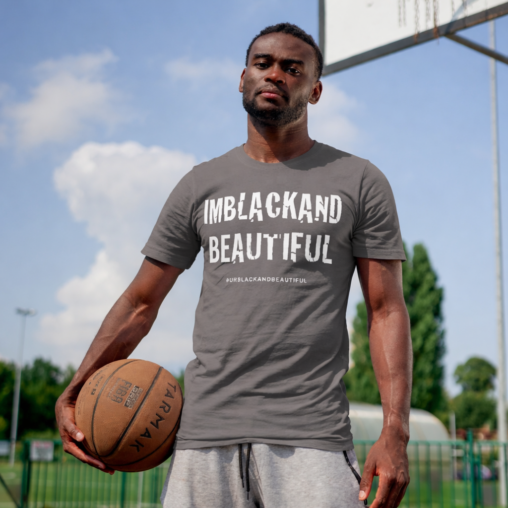 Man holding a basketball wearing a gray t-shirt with 'IMBLACKAND BEAUTIFUL' text on a sports court.