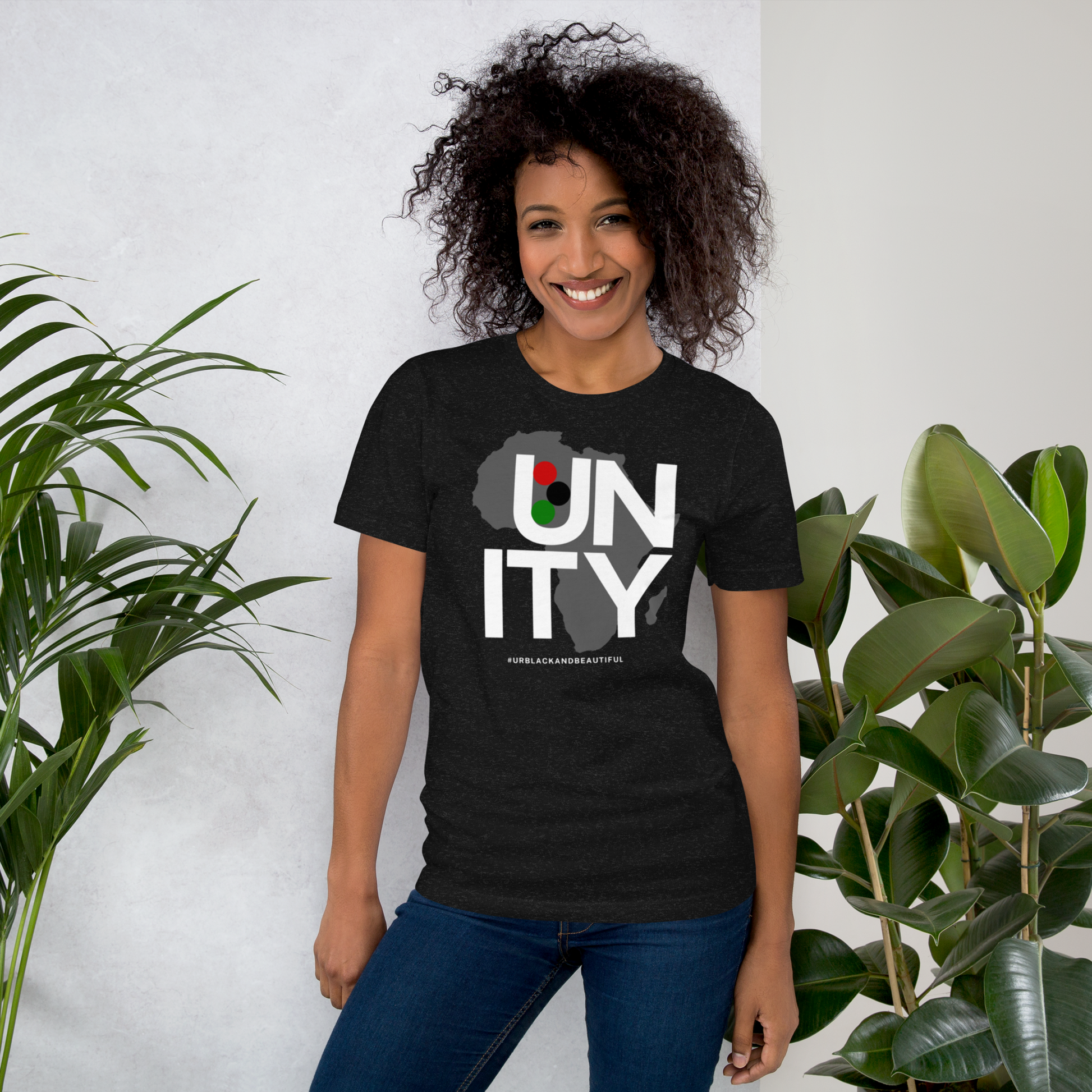 Woman wearing a black t-shirt with 'UNITY' design, standing between two plants.