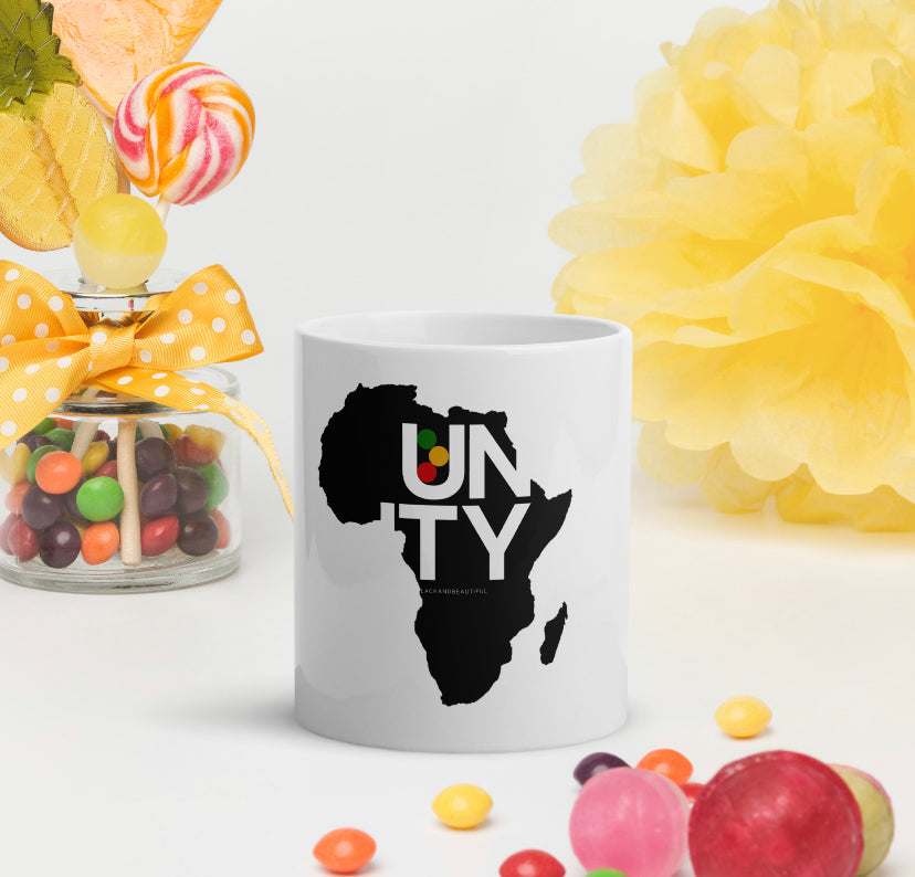 White mug with a black Africa map design and 'UNITY' text, surrounded by colorful candies and flowers.